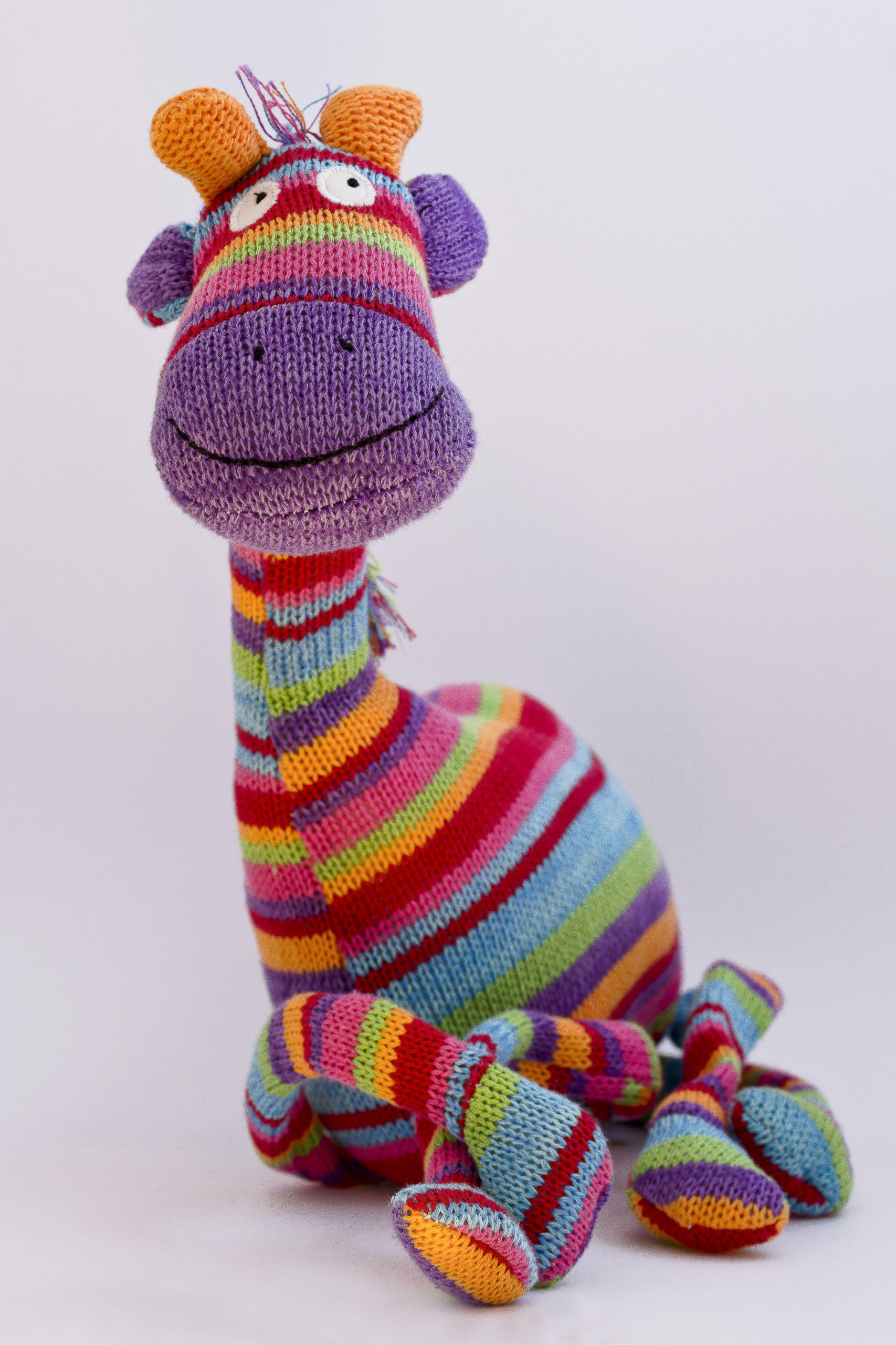 Une peluche de girafe tricotée aux rayures multicolores, posée sur un fond épuré, symbolisant l'univers de la réflexologie pédiatrique pour bébés et enfants.
