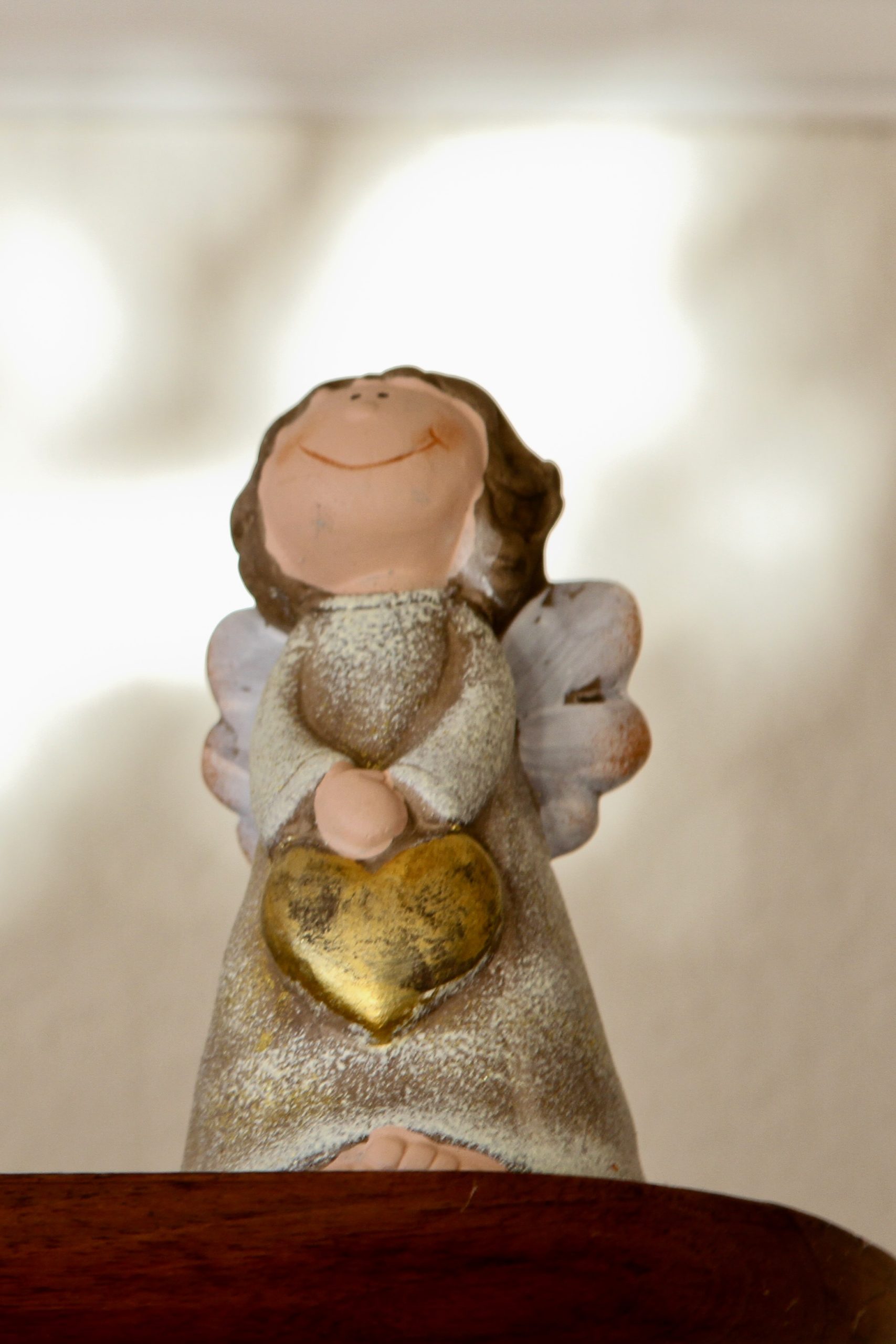Statuette d'ange de la fertilité en céramique avec un cœur d'or symbolique, posée sur une étagère en bois